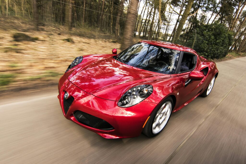 A sleek red sports car driving fast on a forest road, showcasing speed and luxury.